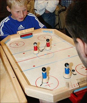 Zwei Kinder spielen Tischhockey auf einem Holzspielbrett mit roten und blauen Figuren.