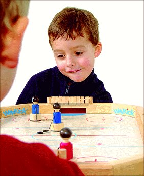 Junge spielt Eishockey mit einem Erwachsenen an einem Tisch.