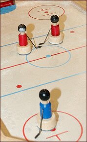 Drei Holzkegel mit Kugeln auf einem Tischhockeyfeld, zwei rote und eine blaue Figur.