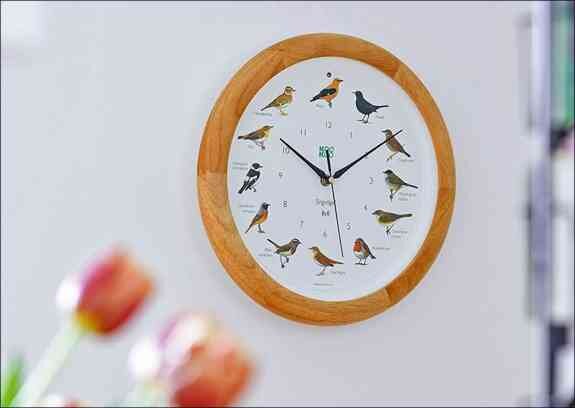 Runder Wand-Uhr mit Vogelmotiven und schwarzen Uhrzeigern an weißer Wand.