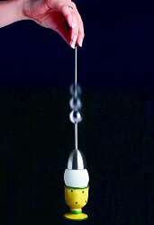 Hand hält eine Pendeluhr mit gelbem Sockel und weißen Oberteil, schwingend gegen schwarzen Hintergrund.