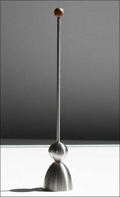 Pendel mit Metallbasis, langer Stab und kleiner Holzball an der Spitze, vor grauem Hintergrund.