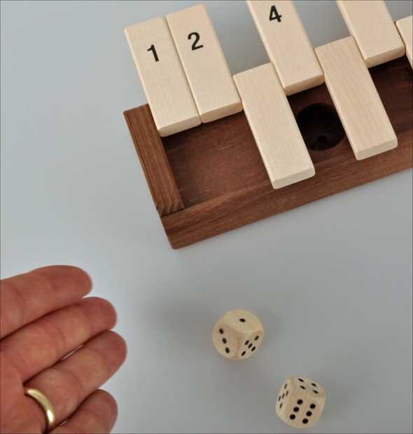 Holzblockpuzzle mit nummerierten Teilen, zwei Würfel mit Punkten, Hand mit Goldring.