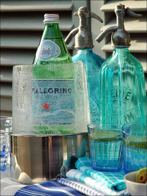 Bunte Wasserflaschen, Gläser mit Zitronen, Eiswürfel und Papiertücher auf einem Tisch.