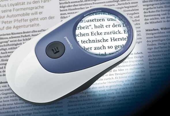 Handlupe mit Vergrößerungsglas über einem Zeitungsartikel, Fokus auf Text.
