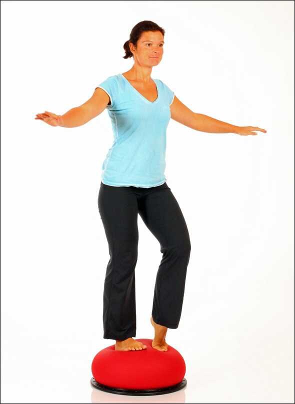 Frau steht auf einem roten Balance-Board mit ausgestreckten Armen, in einer blauen T-Shirt und schwarzen Hosen.