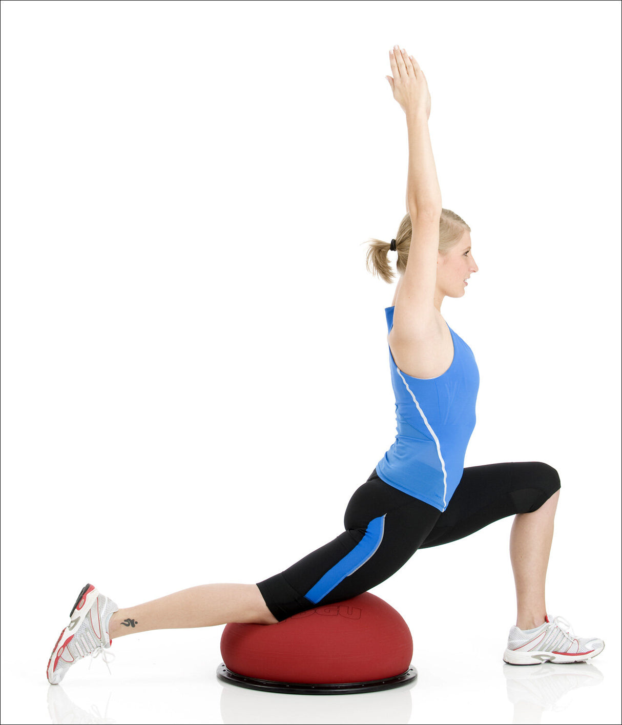 Frau in Sportkleidung macht Yoga-Übung auf Balance- und Fitnessball, mit einem Arm nach oben gestreckt.