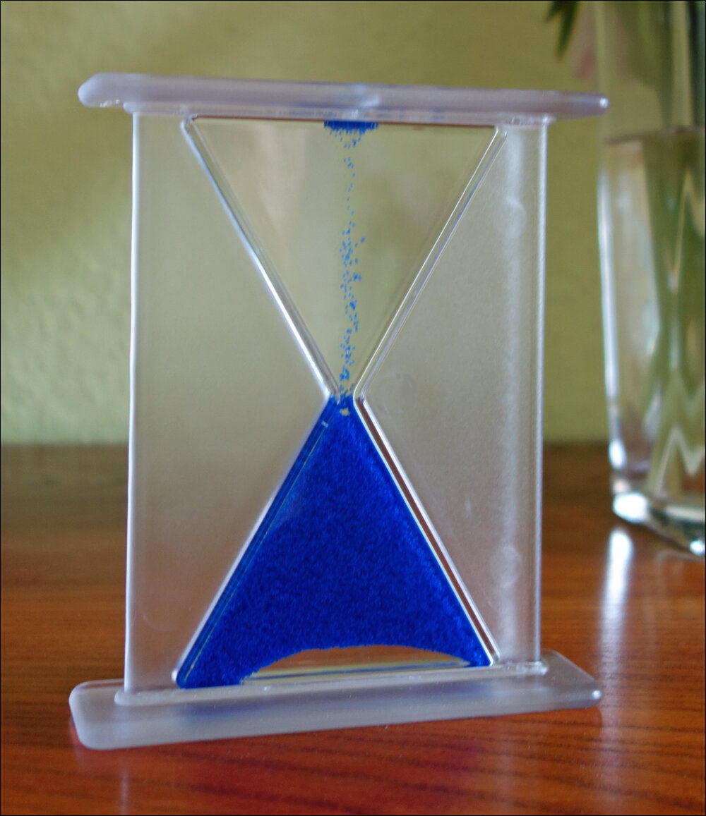 Sanduhr mit blauer Sandkörnern, die durch die Mitte nach unten fließen.