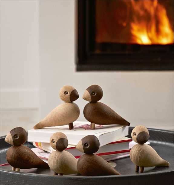 Sechs Holzvögel auf einem Tablett, vor einem Kaminfeuer.