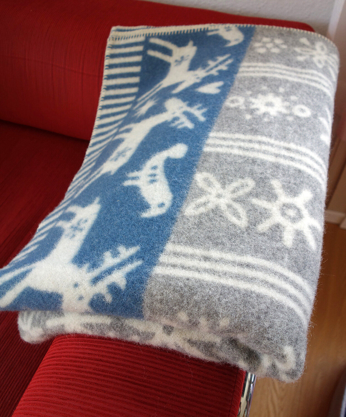 Flauschige Decke mit Weihnachtsmotiven, darunter Elche, Schneeflocken und Sterne, in Blau, Grau und Weiß.