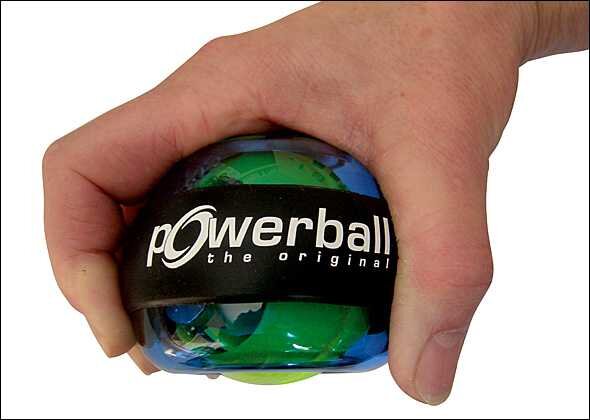 Hand hält einen kleinen, bunten Powerball mit schwarzem Gummiband, auf dem "powerball the original" steht.