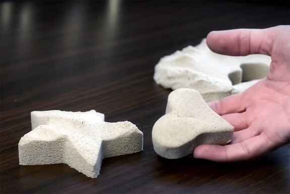 Hand hält zwei große, unregelmäßig geformte, weiße Schaumstoffstücke auf einer dunklen Oberfläche.