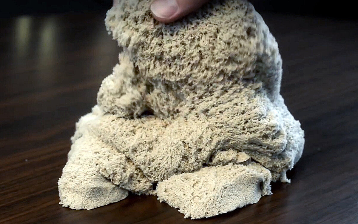 Hand formt einen Klumpen Mehl oder Teig auf einem dunklen Holzuntergrund.