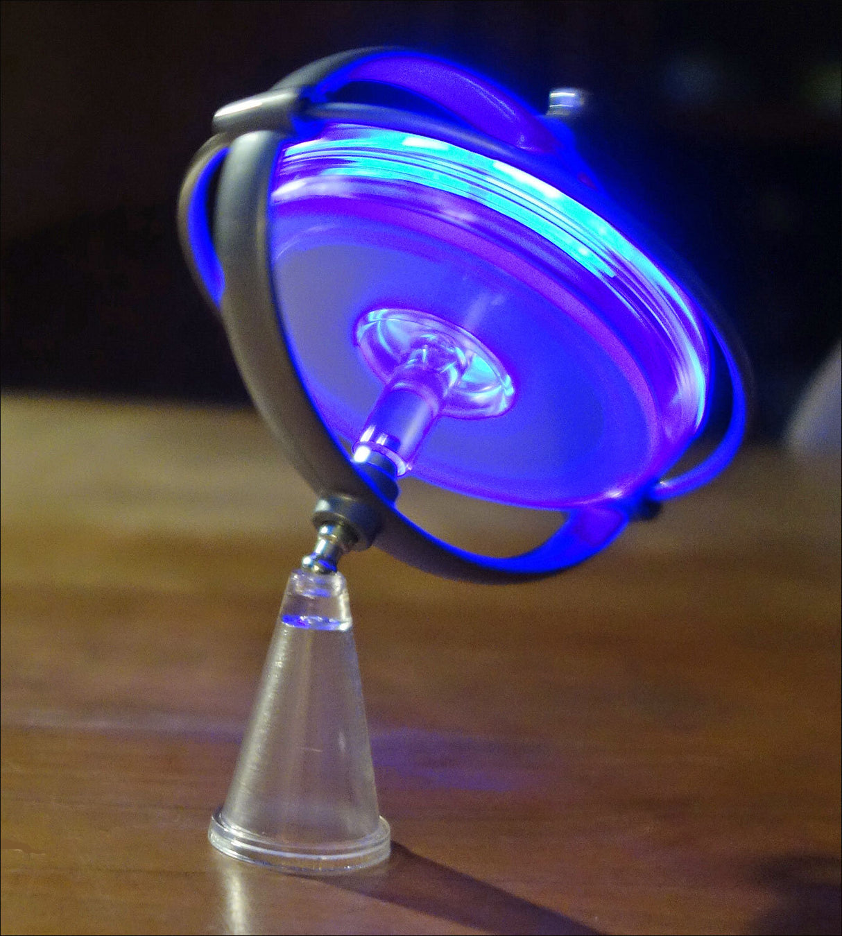 Gerät mit blauer LED-Beleuchtung, auf einem Holzuntergrund, mit einer kleinen Glasflasche darunter.