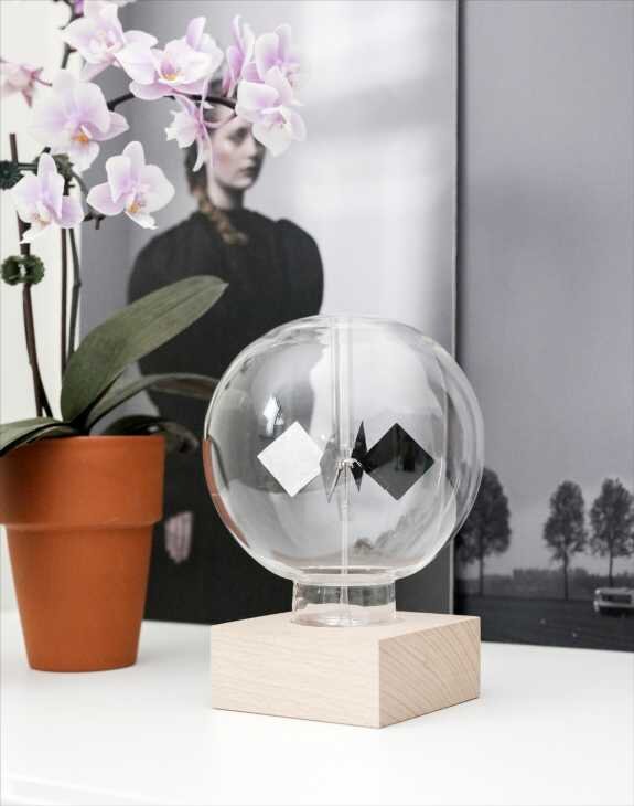 Glasballon mit schwarzem und weißem geometrischem Muster auf Holzsockel, Orchidee in Topf, Schwarz-Weiß-Foto im Hintergrund.