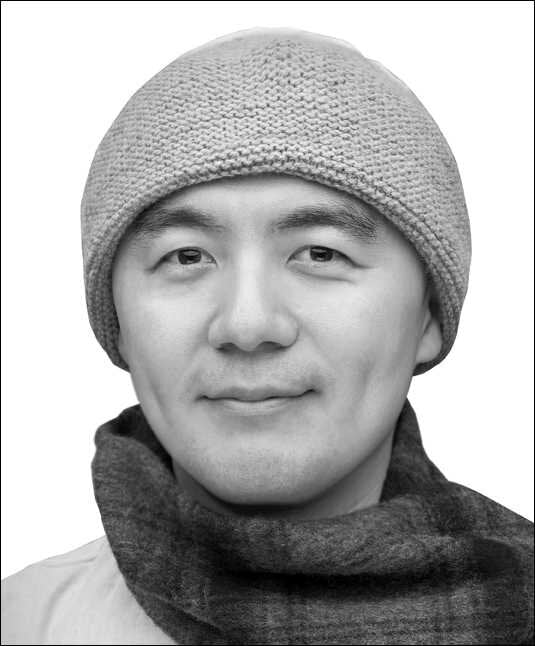 Schwarz-weißes Portrait eines Mannes mit Mütze und Schal, lächelnd, frontal fotografiert.