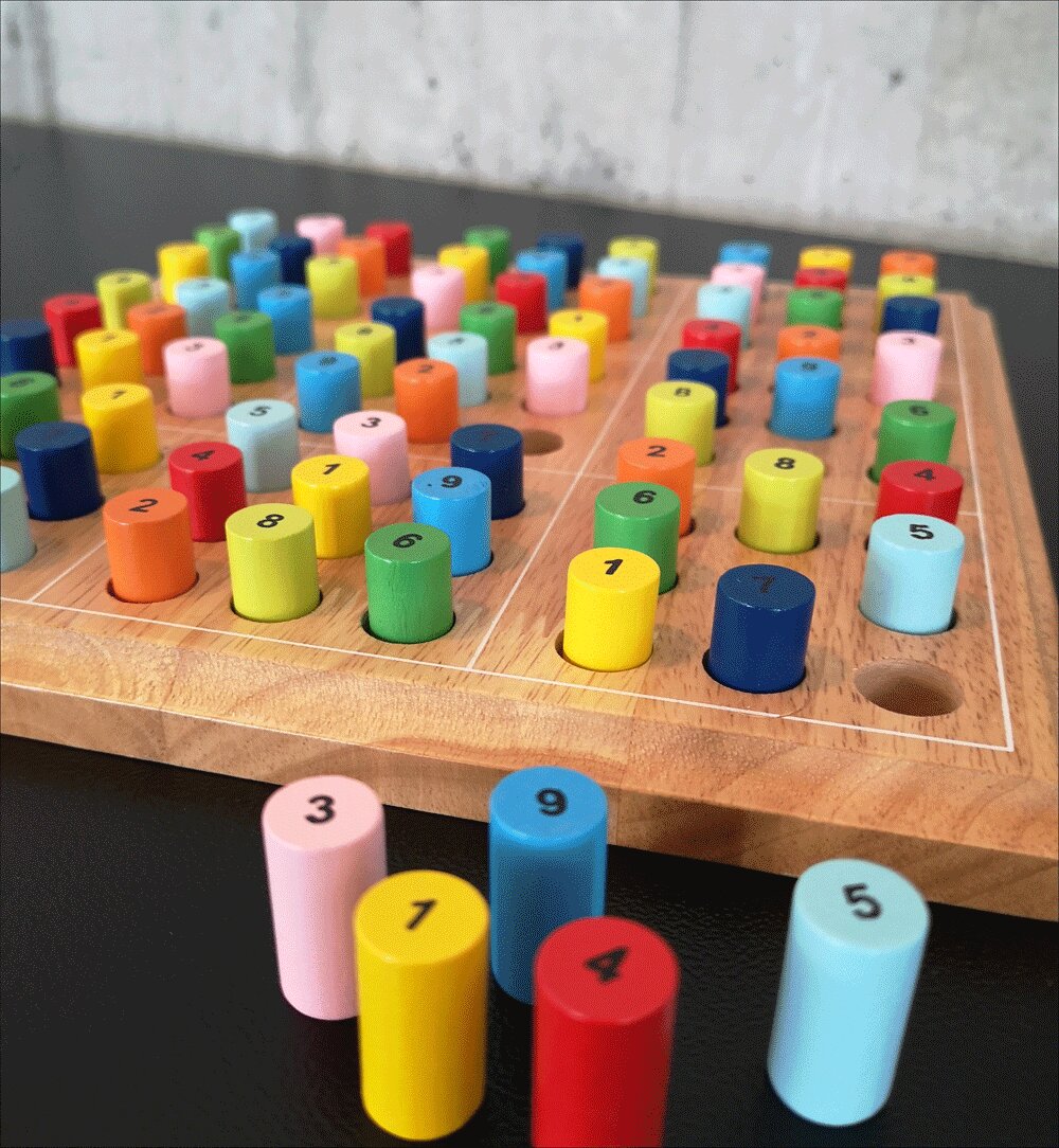 Bunte, nummerierte Holzstäbchen auf einem Spielbrett mit Löchern, sortiert nach Farben und Zahlen.