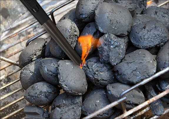 Rauchende Kohlebriketts auf einem Grill, mit einem Feuerzeug entzündet.
