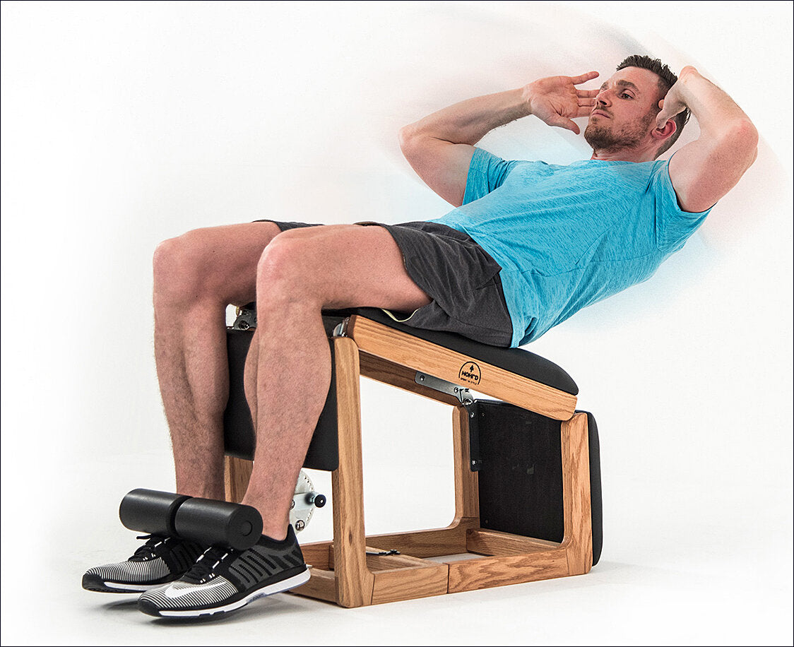 Mann liegt auf einem Pilates-Reformer, entspannt mit Händen hinter dem Kopf, trägt ein blaues T-Shirt und schwarze Shorts.