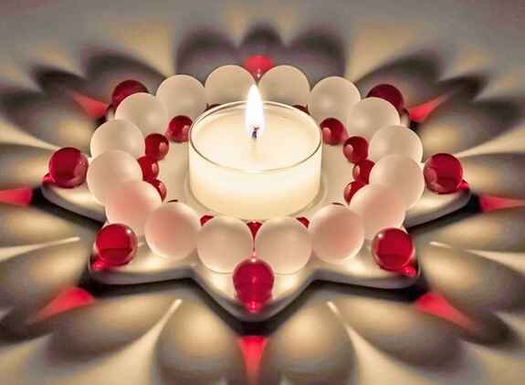 Teelicht in der Mitte, umgeben von weißen und roten Kugeln, auf einer mehrschichtigen, blumenförmigen Anordnung.