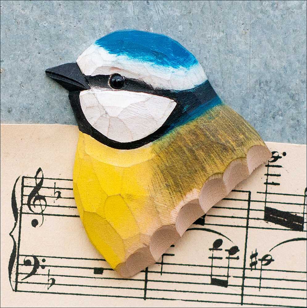 Holzschnitt eines bunten Vogelkopfs auf Notenblatt, mit blauer, weißer, schwarzer und gelber Farbgebung.