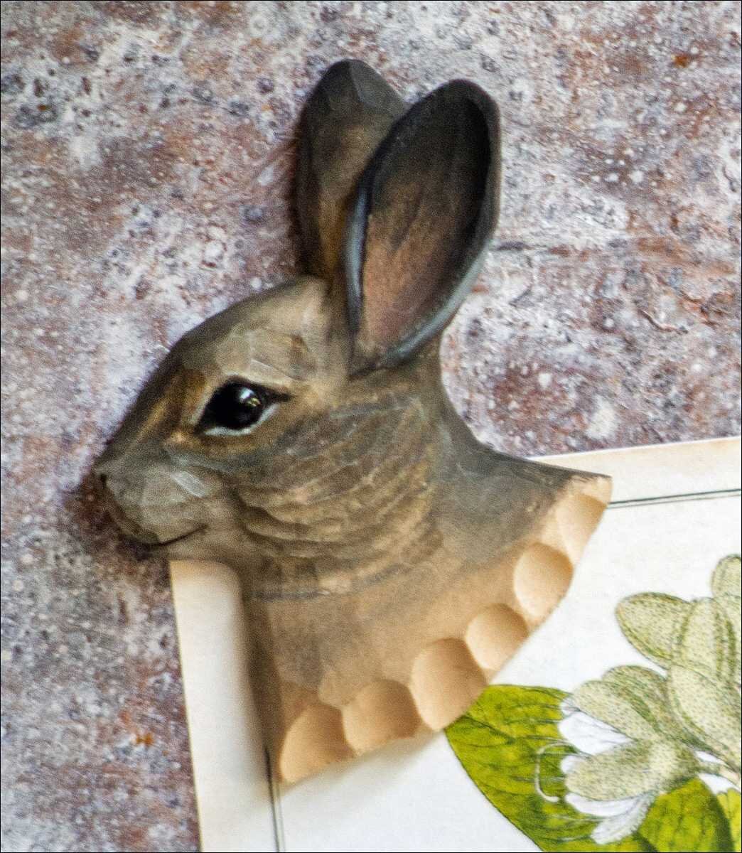 Holzschnitt eines Hasen mit großen Ohren, auf einer Stein- oder Fliesenfläche.