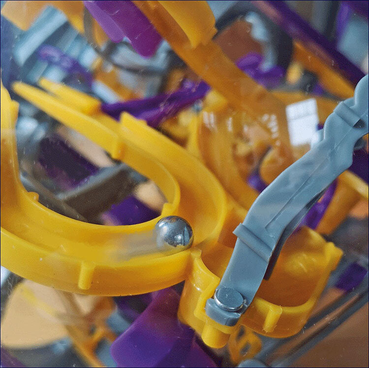 Bunte Kunststoff- und Metallteile in einem Spielzeug- oder Baukasten-Set, hauptsächlich in Gelb, Lila und Grau.