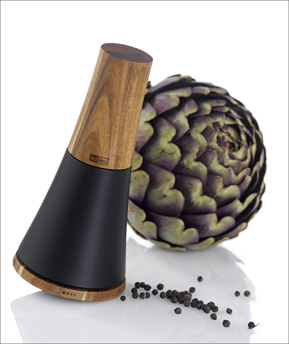 Elektrischer Pfeffermühle mit Holz- und schwarzen Kunststoffteilen, Artischocke und Pfefferkörner im Hintergrund.