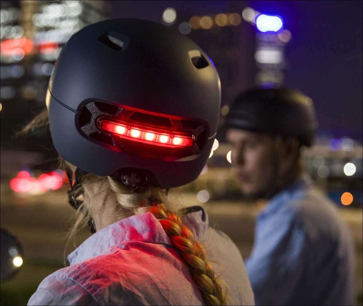 Zwei Personen mit Helmen, eine trägt einen schwarzen Helm mit rotem Rücklicht, die andere einen schwarzen Helm, bei Nacht.