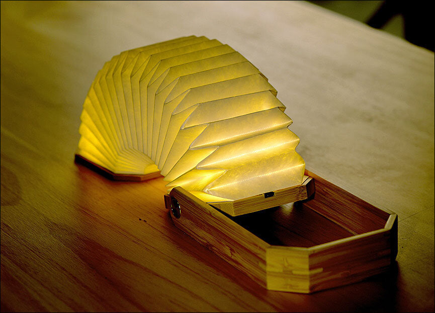Leuchtende, faltbare Lampe in einer Holzbox auf einem Holztisch.