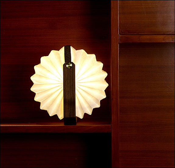 Heller, gefalteter Lampenschirm an einer dunklen Holzoberfläche.