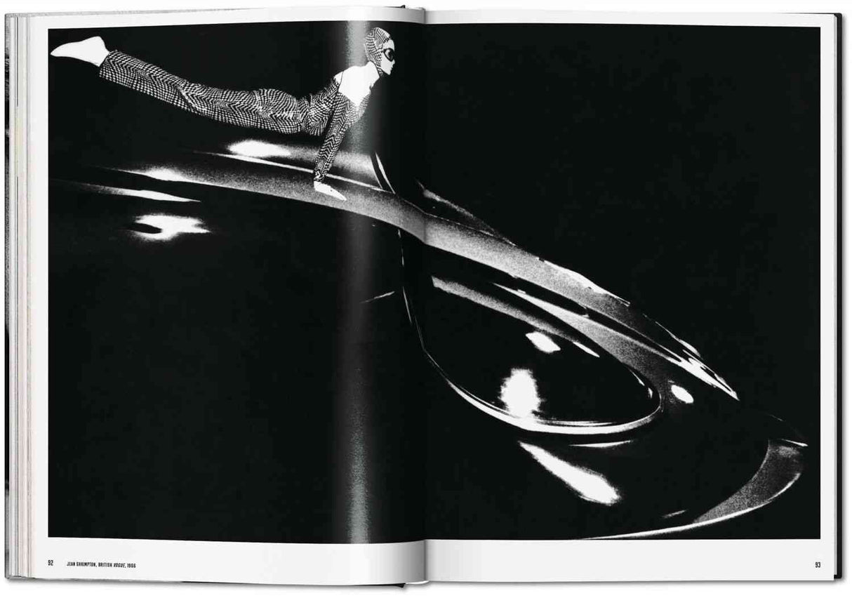 Schwarzes und weißes Bild eines Menschen in einem Anzug, der auf einem großen, glänzenden, ovalen Objekt balanciert.