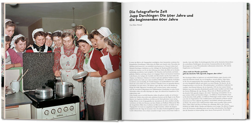 Mehrere junge Frauen in Küchenkleidung und Hauben schauen auf einen Herd mit Töpfen.
