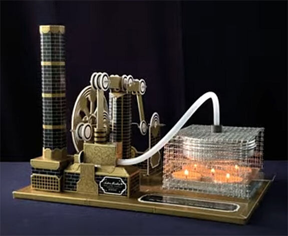 Kleines Modell einer Stadt mit Gebäuden, Zahnrädern, einer Wasserleitung und einem transparenten Container mit Kerzen.