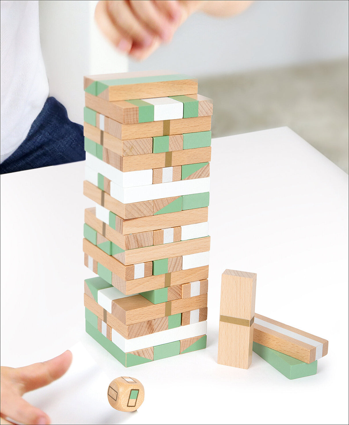 Mehrstöckiger Jenga-Turm aus Holz mit grünen, weißen und natürlichen Holzfarben, daneben ein Würfel und zwei einzelne Holzklötze.