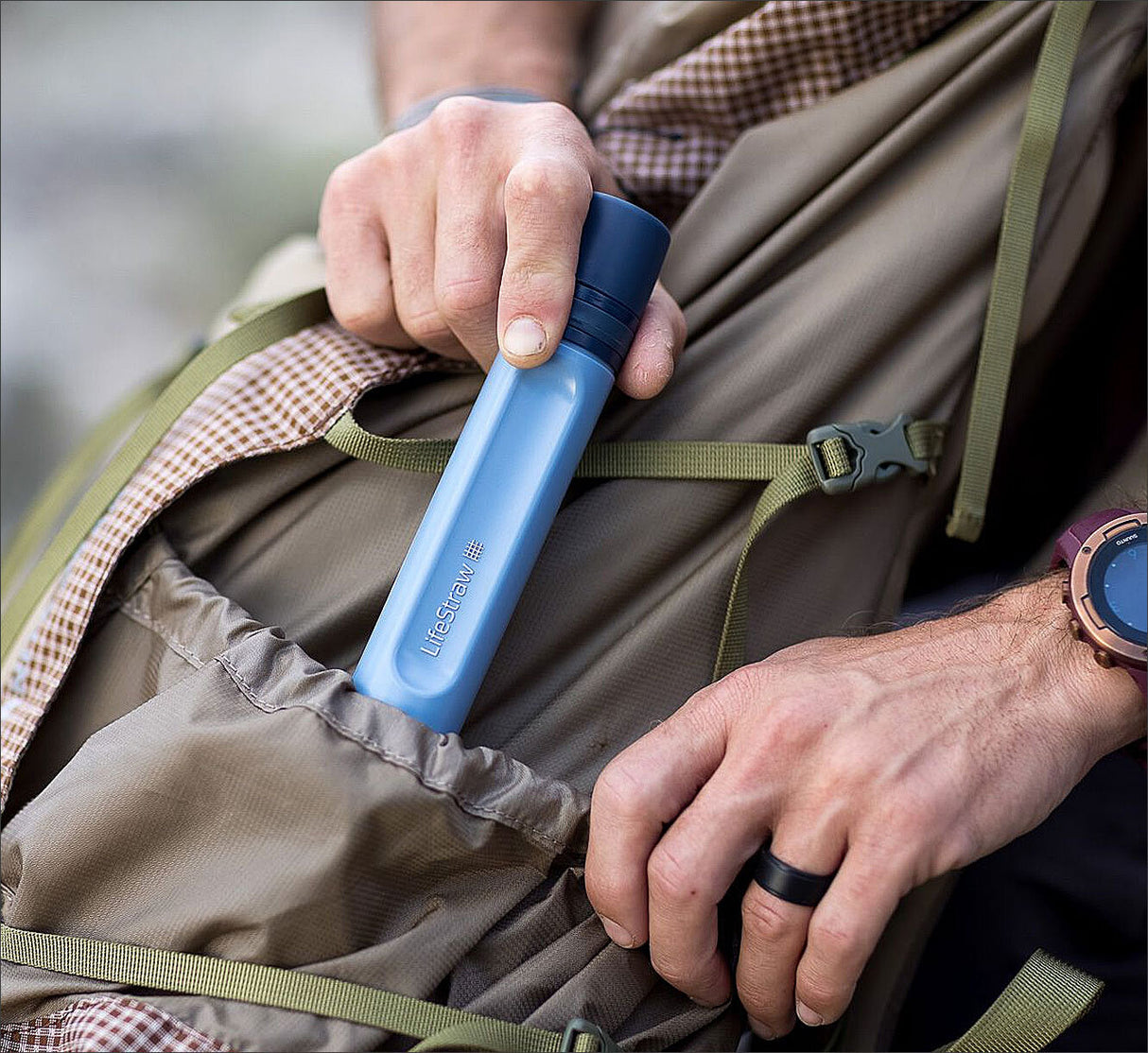 Hand, die eine blaue Trinkflasche mit der Aufschrift "LifeStraw" aus einem Rucksack zieht.