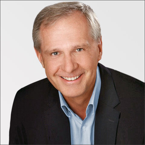 Ein lächelnder Mann mit kurzen, grauen Haaren, trägt einen schwarzen Anzug und eine hellblaue Hemd.