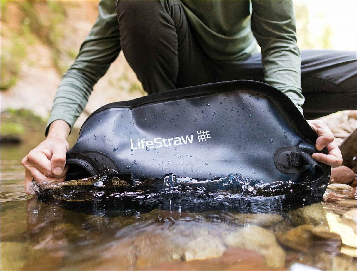 Person hält eine schwarze, wasserdichte Tragetasche mit der Aufschrift "LifeStraw" im Wasser.