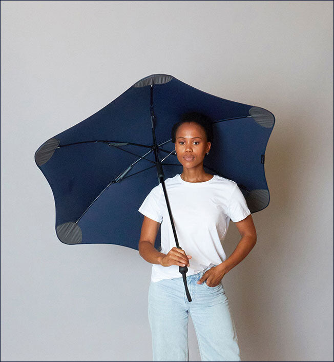 Frau hält einen offenen blauen Regenschirm vor einem grauen Hintergrund.