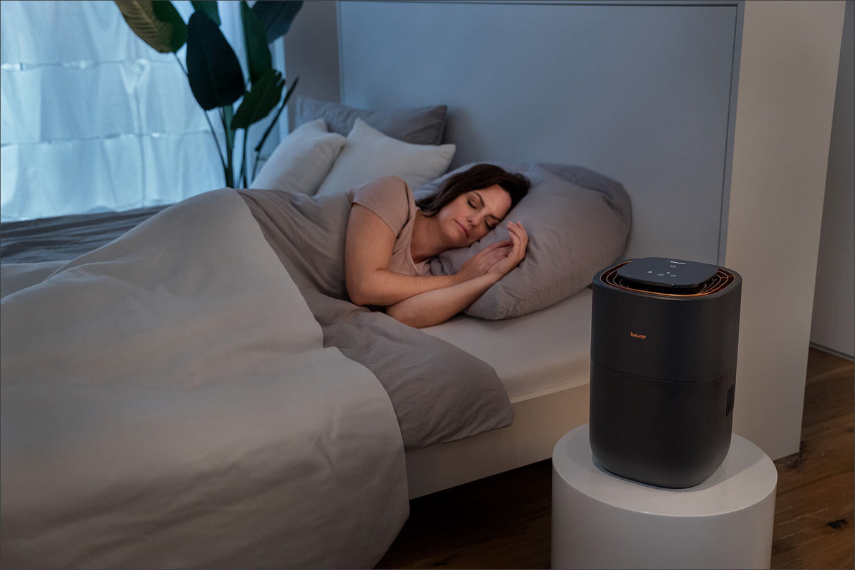 Frau schläft im Bett, neben einem Luftreiniger auf einem weißen Tisch.