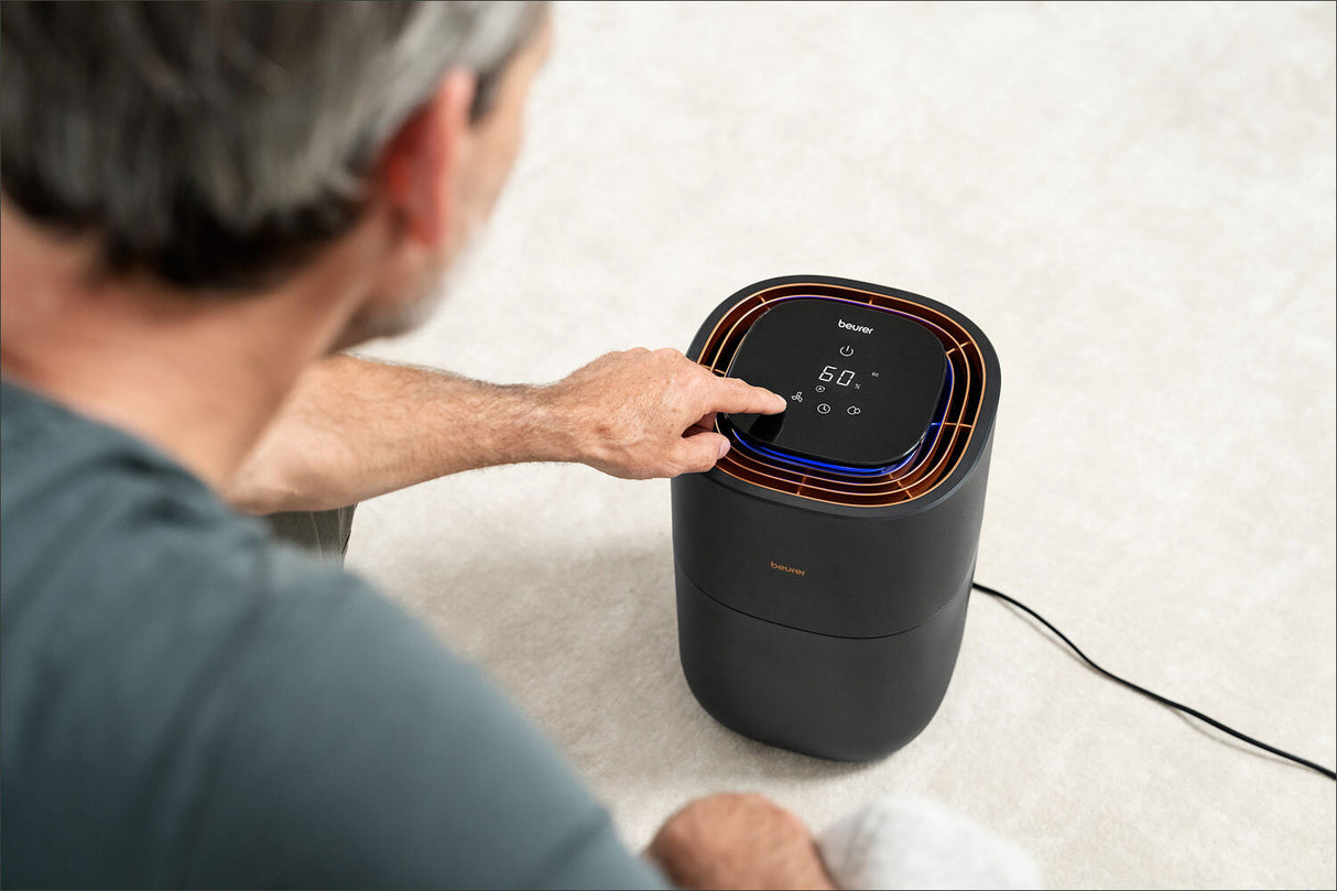 Älterer Mann bedient einen Luftreiniger mit Touchscreen-Display auf dem Boden.