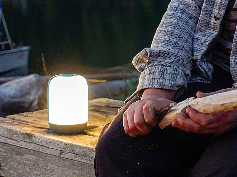 Person schneidet Holz bei Dämmerung, neben einem tragbaren, leuchtenden Lampen auf einem Holzblock.