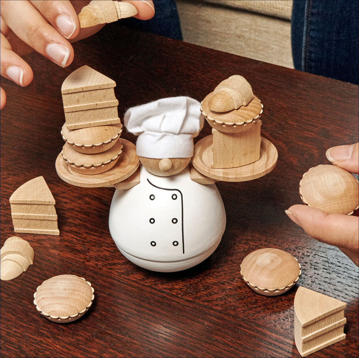 Kochfigur mit Holzplatten, auf einem weißen, kochmütze- und kochjacke-Design. Hände platzieren Holzstücke auf der Figur.