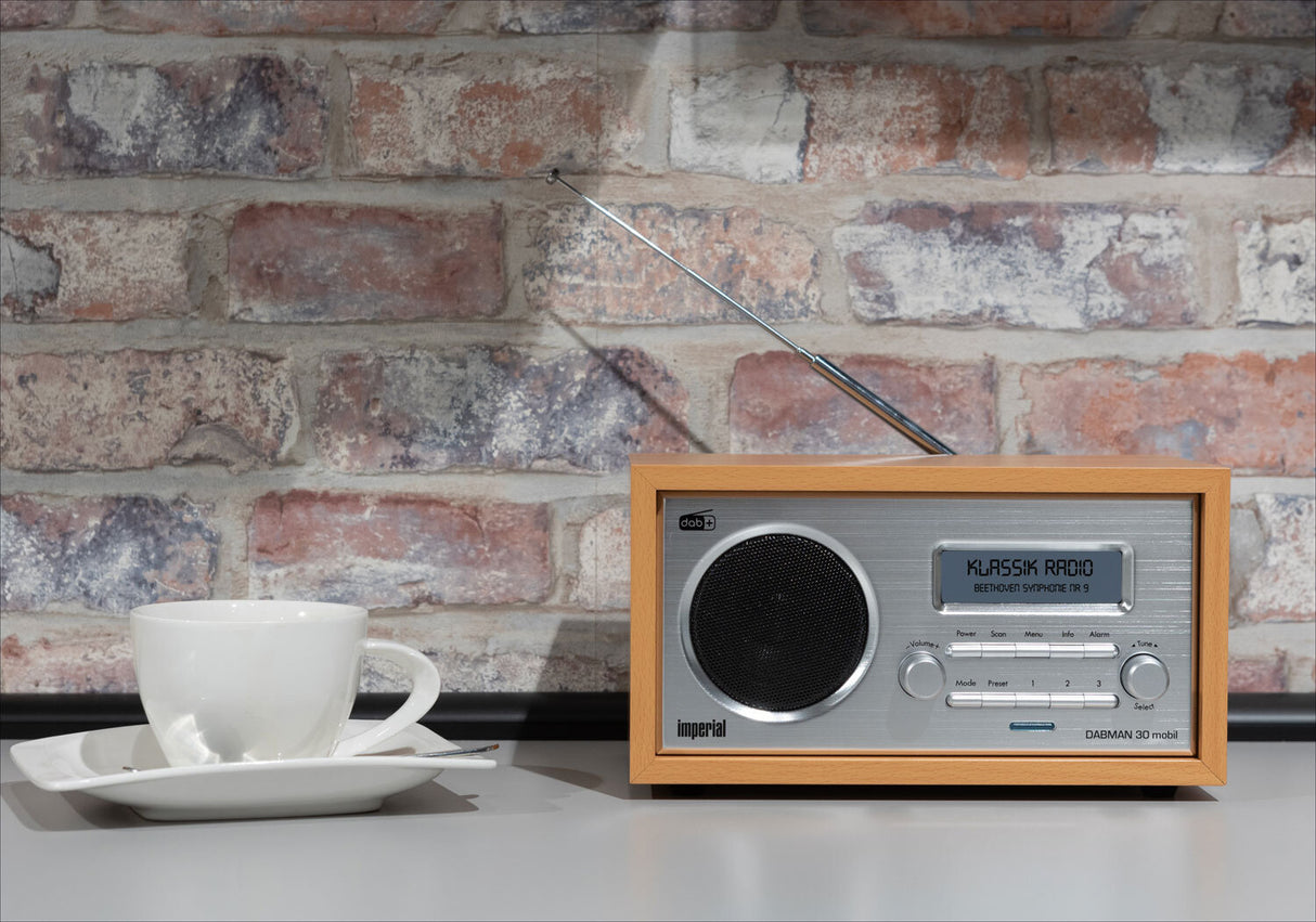 Kleiner Radiowecker, weiße Tasse auf weißem Teller, gegen Backsteinwand.