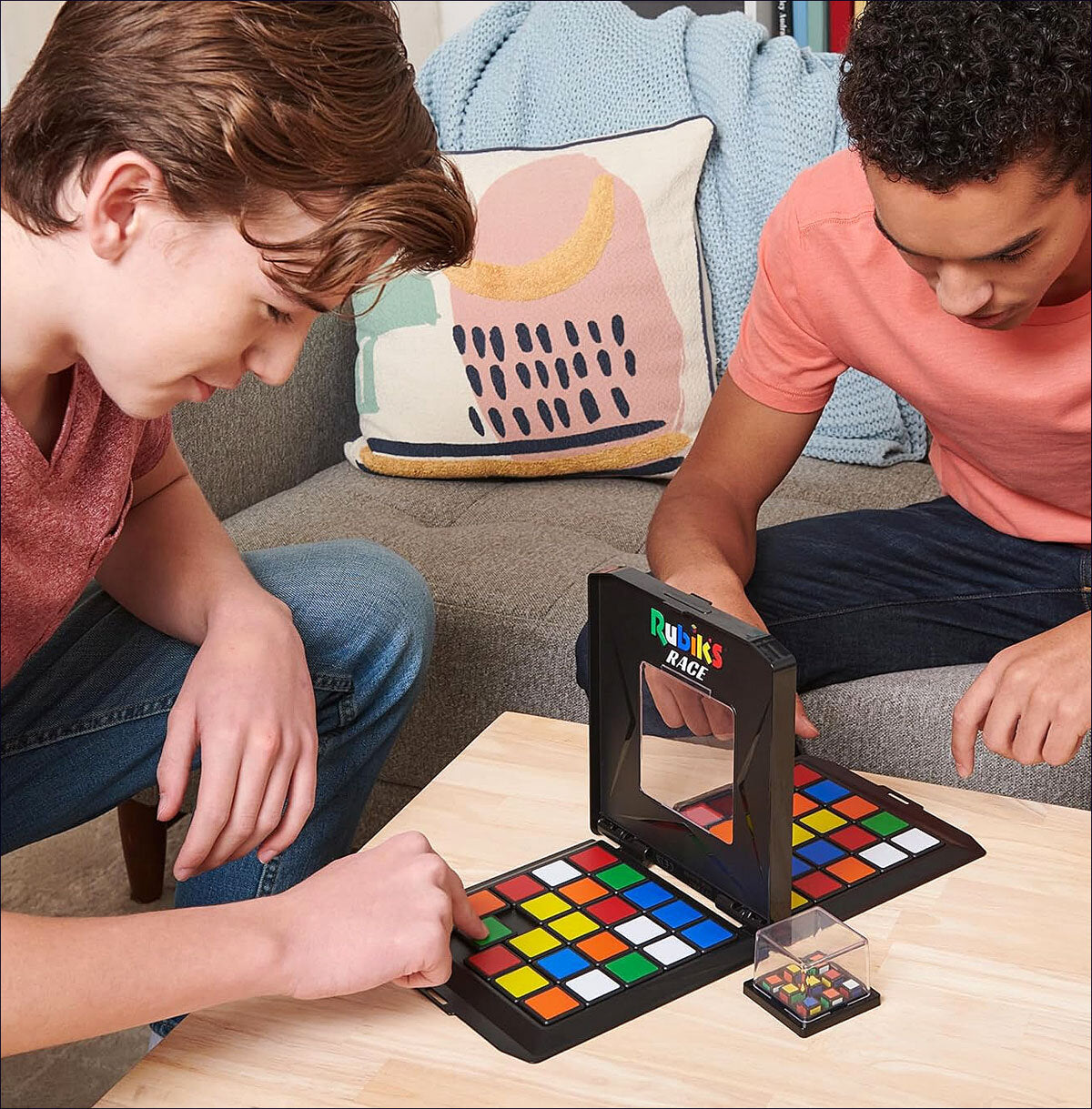 Zwei junge Männer spielen mit einem Rubik's Cube Race Spiel auf einem Tisch.