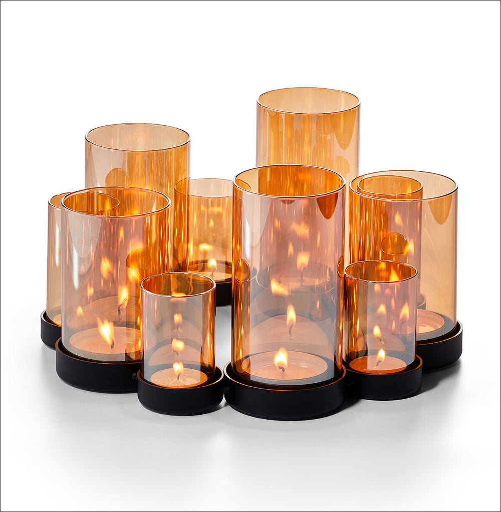 Mehrere brennende Kerzen in orange-transparenten Glasvasen auf schwarzem Untersetzer.