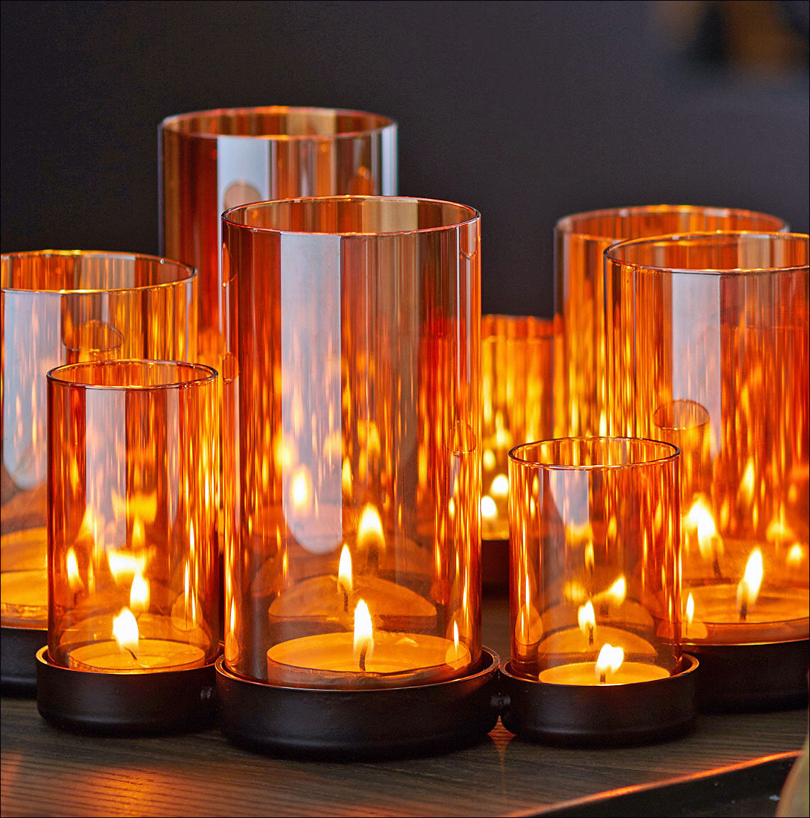 Mehrere brennende Kerzen in orangefarbenen Glasvasen auf einer schwarzen Oberfläche.