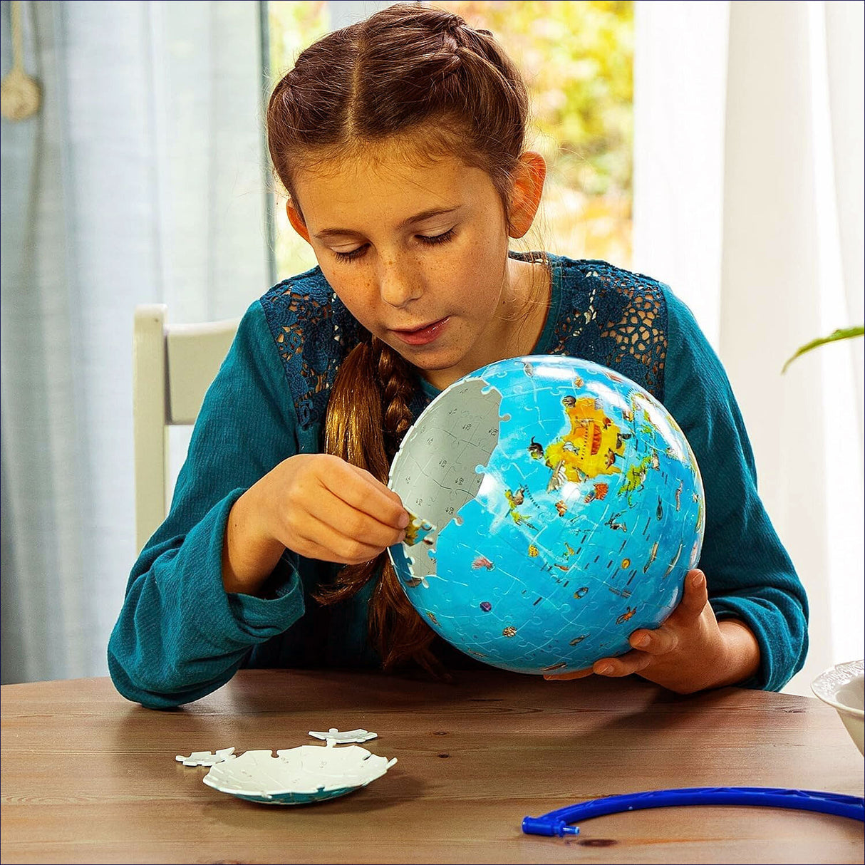 Mädchen puzzelt eine Weltkugel auf einem Tisch, mit Puzzlestücken und einem blauen Werkzeug.