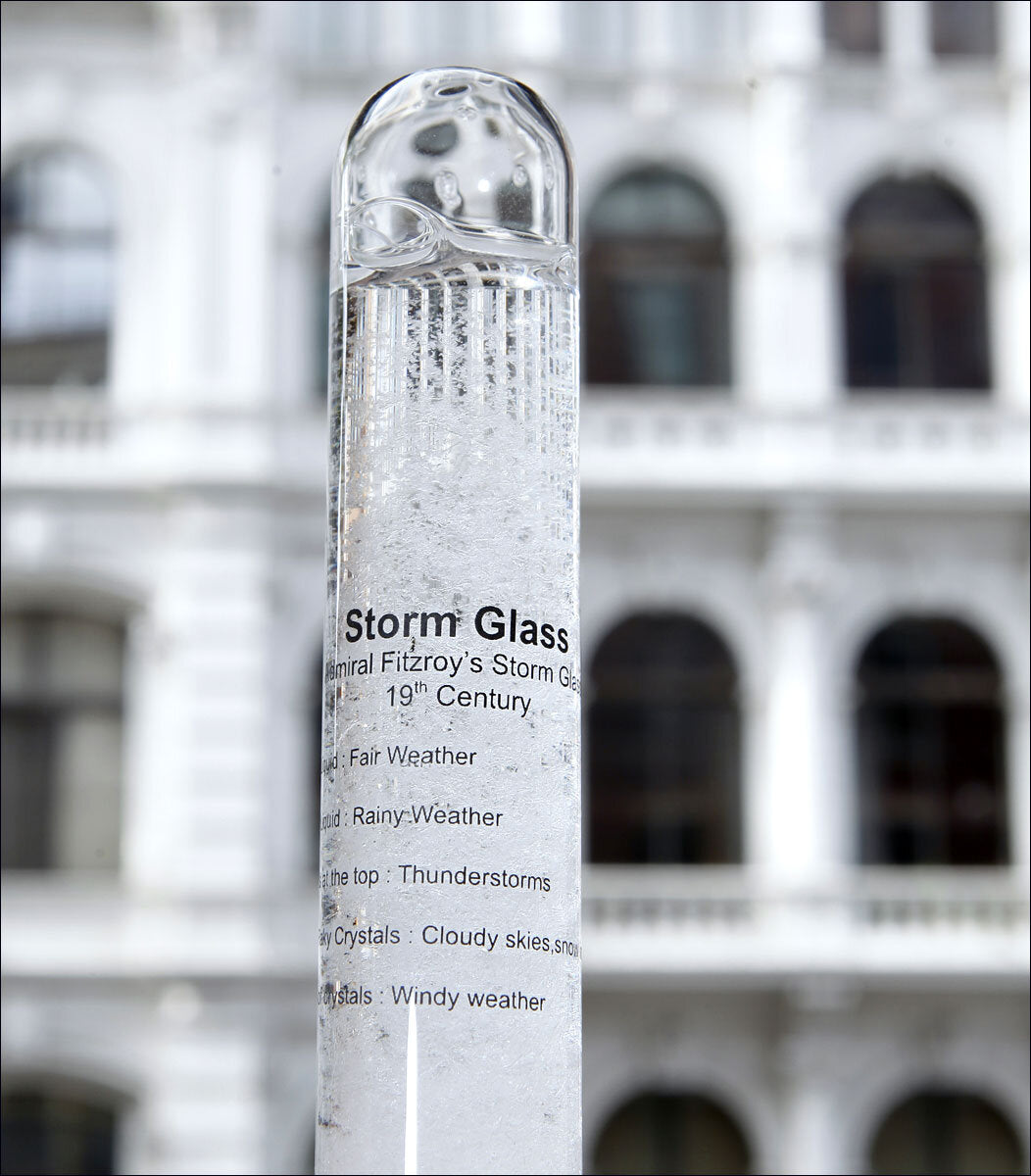 Ein Stormglas mit Wetterbeschreibung, vor einem Gebäude mit weißen Balkonen.