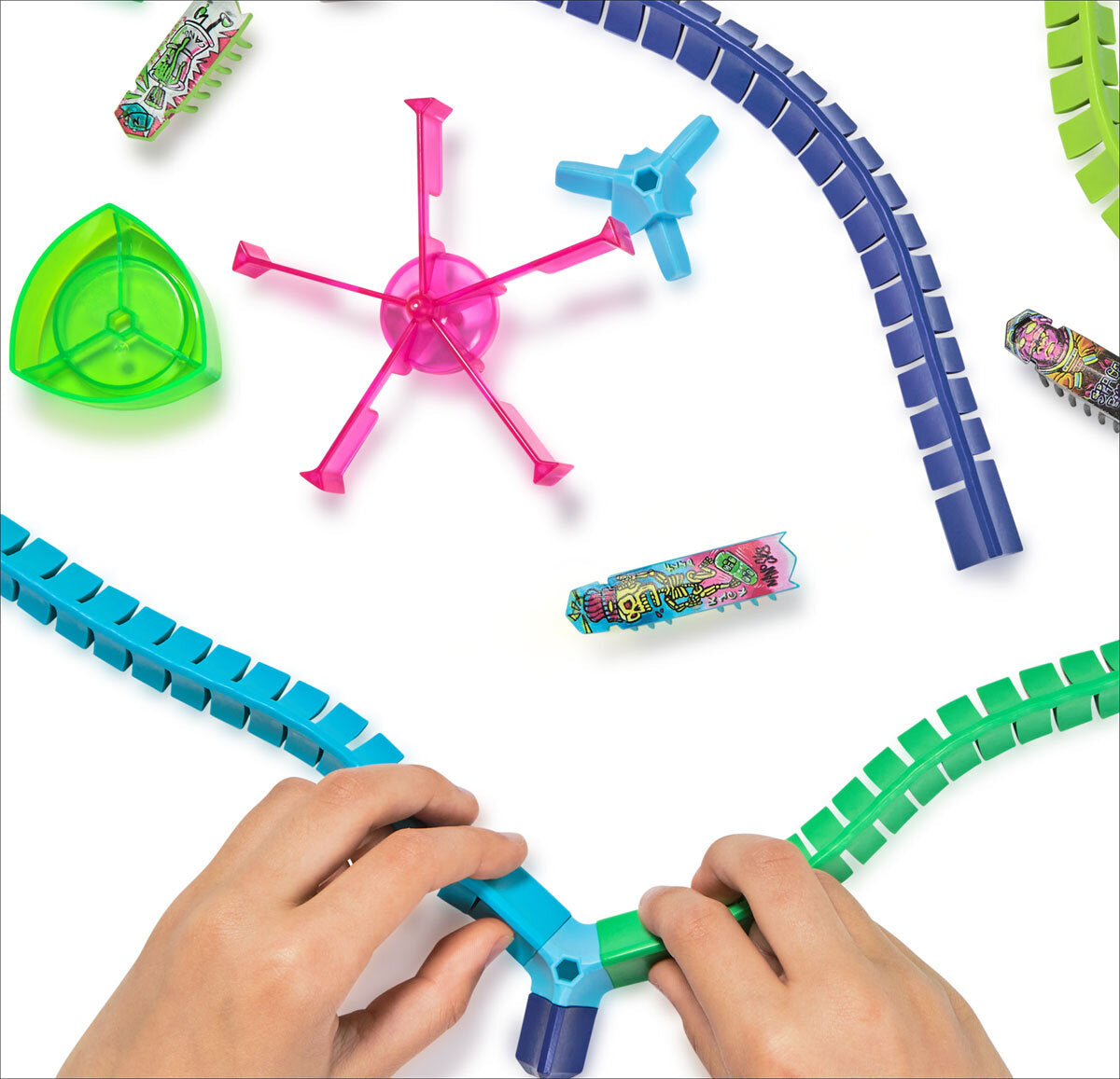 Hände bauen eine Bahn aus bunten, rechteckigen Schienen auf weißem Hintergrund.